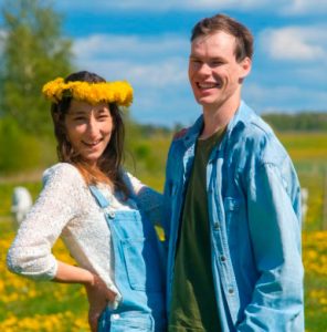 Jauns pāris smaida ziedošā pļavā Kurzemes laukos; sievietei galvā dzeltenu ziedu vainags